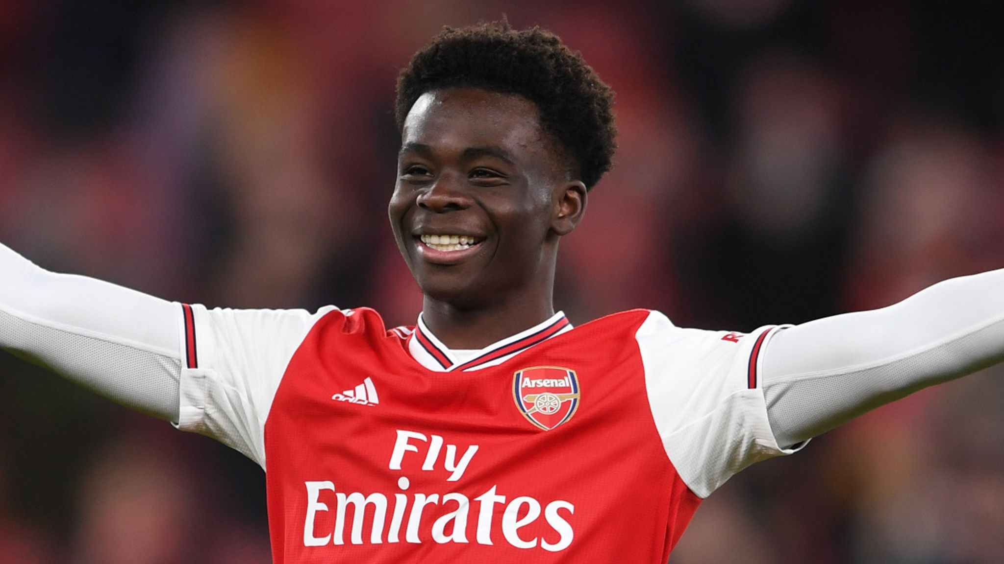  Bukayo Saka, a young Arsenal football player, is celebrating a goal with his arms outstretched.